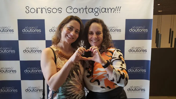 Duas alunas fazendo coração com as mãos em frente ao painel Sorrisos Contagiam